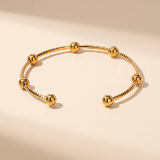 High quality Astrid gold beaded cuff bangle by Floravisha showing mirror-polished spheres and open wire design on a warm beige studio surface.
