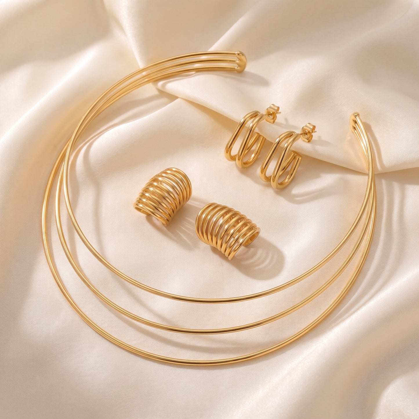 Tarnish-free Aura gold triple band choker necklace styled on champagne silk fabric alongside matching gold ear cuffs and double oval hoops.