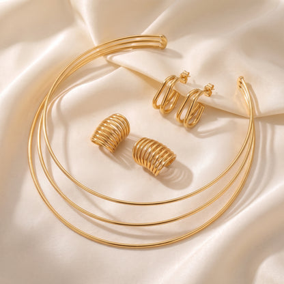 Tarnish-free Aura gold triple band choker necklace styled on champagne silk fabric alongside matching gold ear cuffs and double oval hoops.