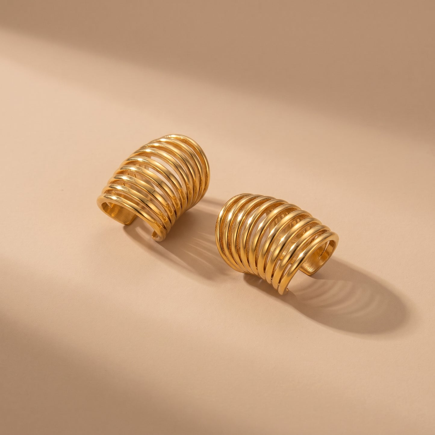 High quality Aura Gold Ear Cuffs by Floravisha featuring 10 parallel ribbed gold bands resting on a warm beige surface under natural sunlight.