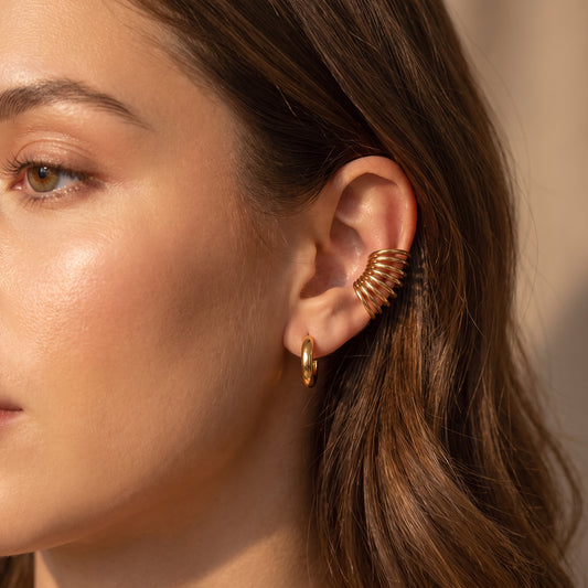 Close-up profile of a woman wearing the skin friendly Aura gold multi-band ear cuff on her ear conch paired with a polished gold hoop.