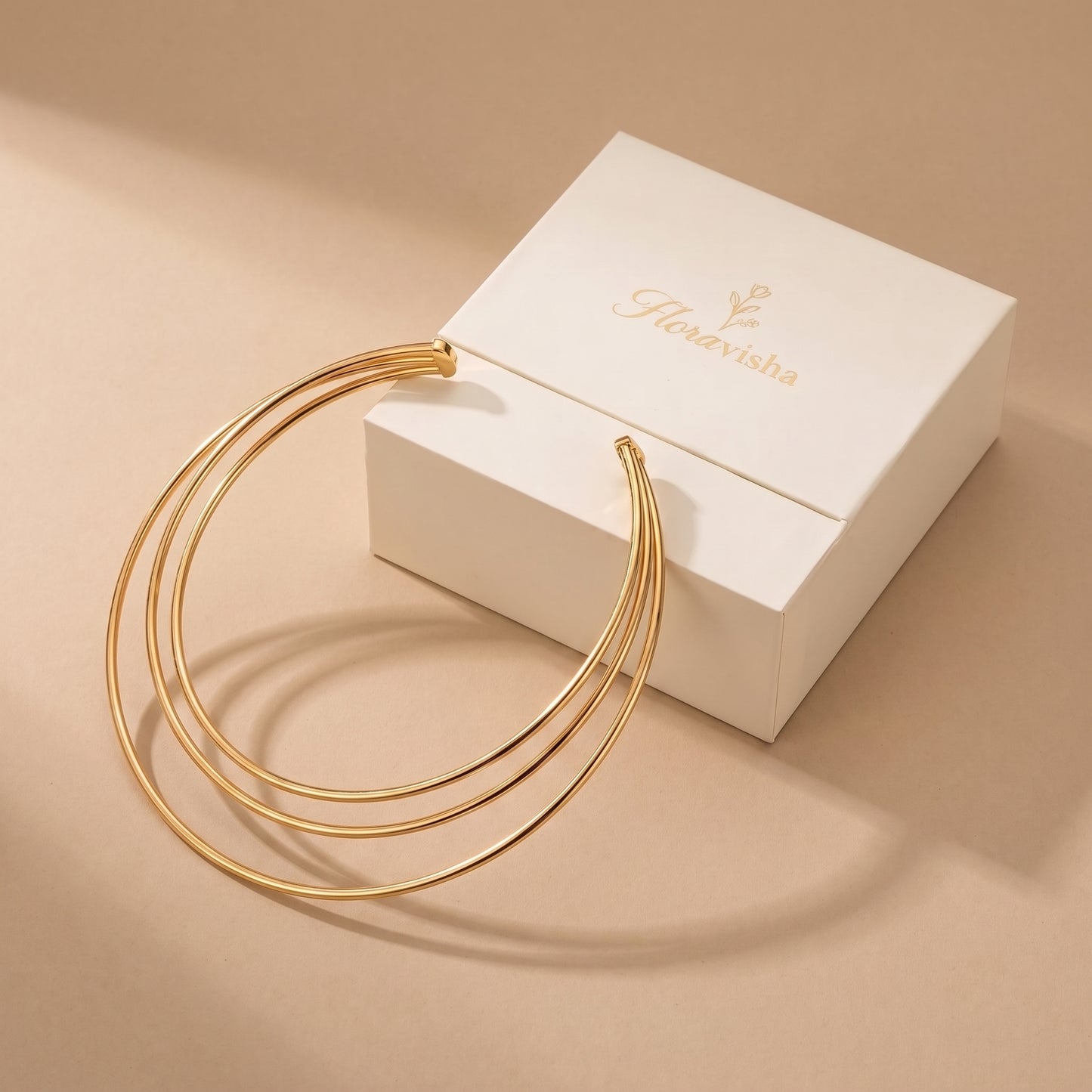 High quality Aura gold triple-band torque choker presented beside an off-white Floravisha luxury sliding jewelry gift box.