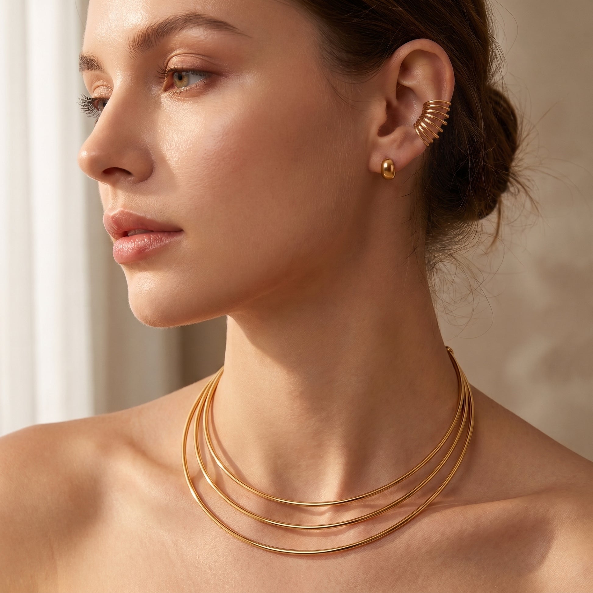 High quality Aura gold triple-band torque choker worn on a model's neck paired with the matching Aura multi-line ear cuff in soft natural lighting.