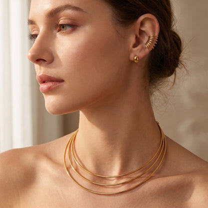 High quality Aura gold triple-band torque choker worn on a model's neck paired with the matching Aura multi-line ear cuff in soft natural lighting.