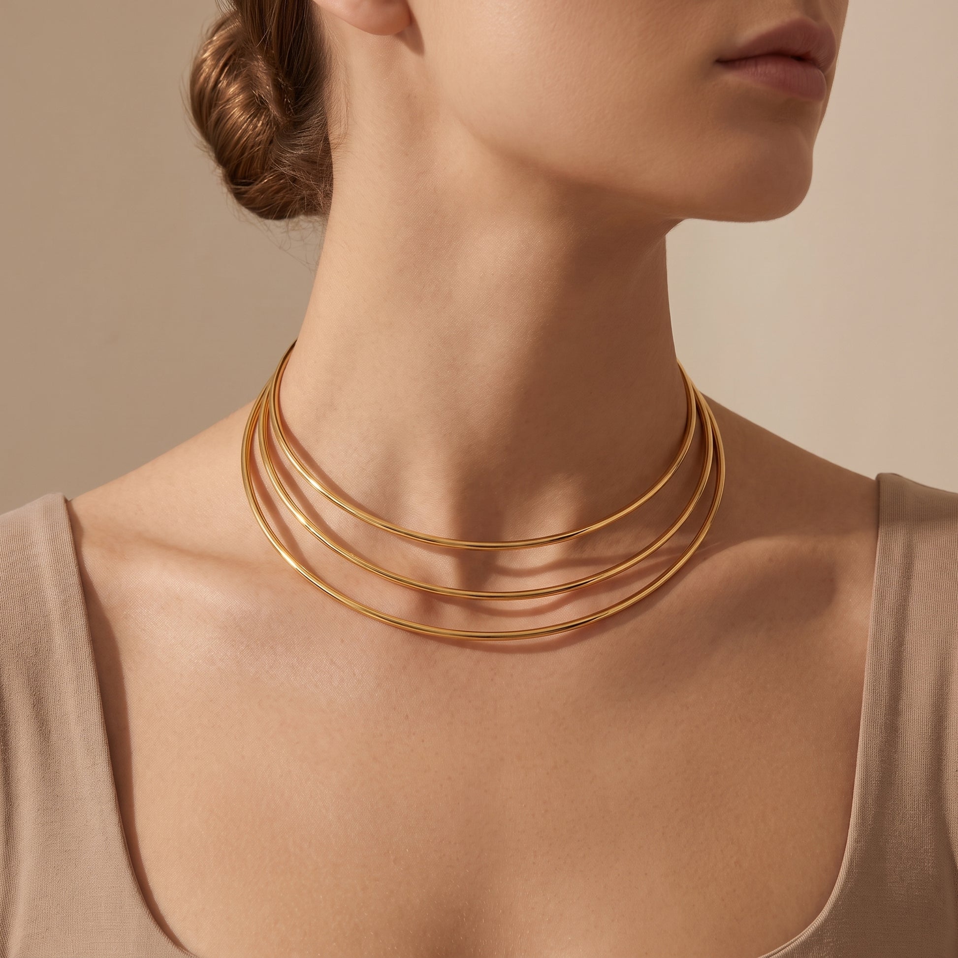 Skin friendly Aura gold triple-strand open torque choker resting flat on a model's collarbone with a neutral beige top.