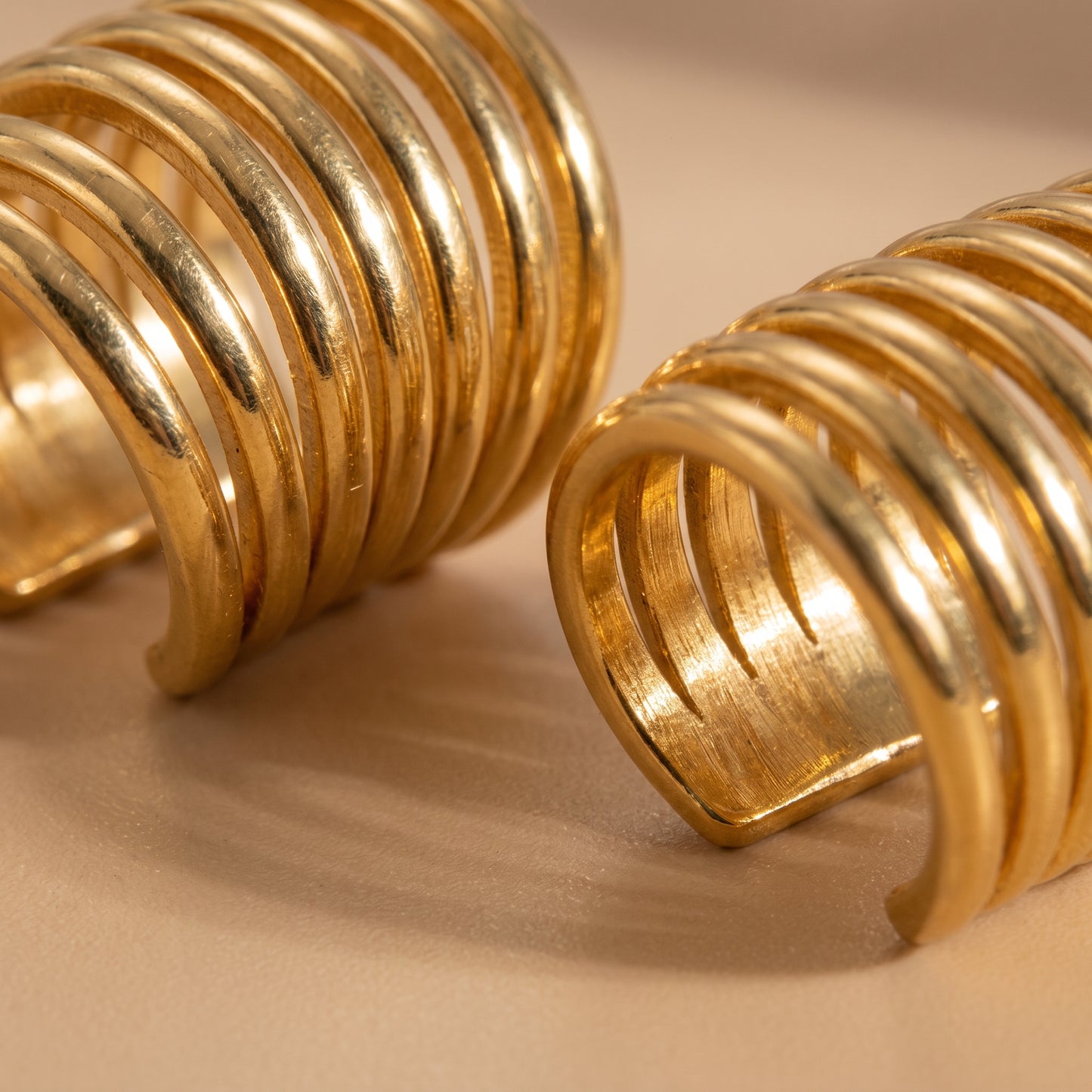 Extreme macro detail view of the tarnish-free Aura gold ear cuffs showcasing the smooth parallel ridges and polished open-cuff silhouette.
