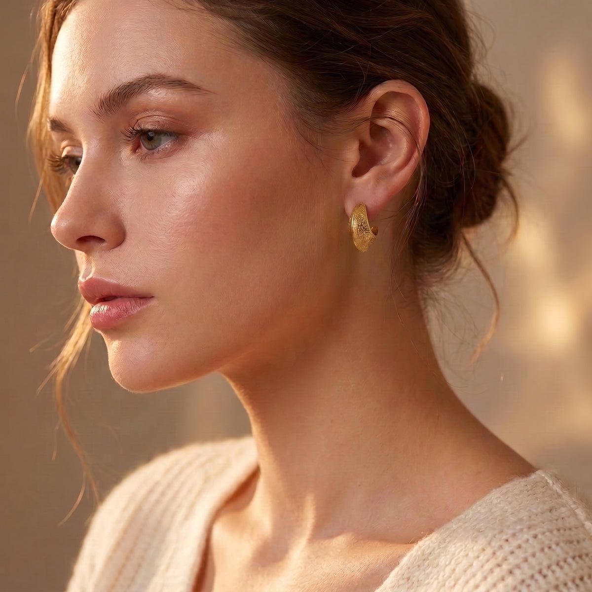 Editorial side portrait of a woman wearing the waterproof Aurelia gold hammered statement crescent hoops framing the jawline in soft studio lighting.