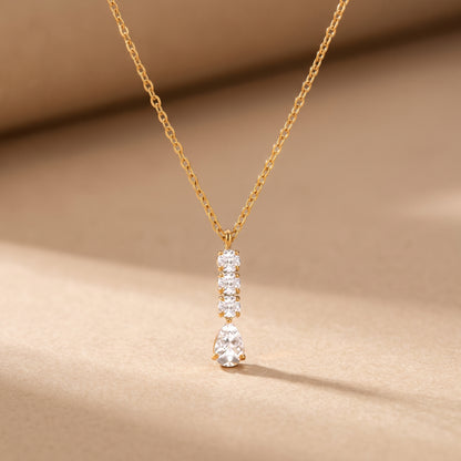 High quality Camille gold linear necklace displaying a vertical column of three round crystals and a suspended pear-cut teardrop pendant on a warm beige studio surface.