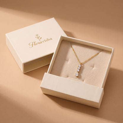High quality Camille gold linear crystal drop necklace presented on a plush velvet pillow inside an off-white Floravisha luxury sliding jewelry gift box.