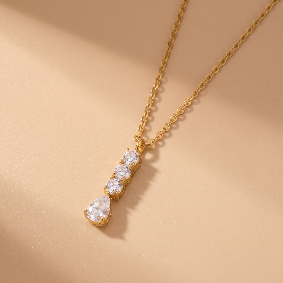 Extreme macro close-up of the tarnish-free Camille gold necklace showing prong-set round brilliant cubic zirconia stones and an articulated pear teardrop crystal.