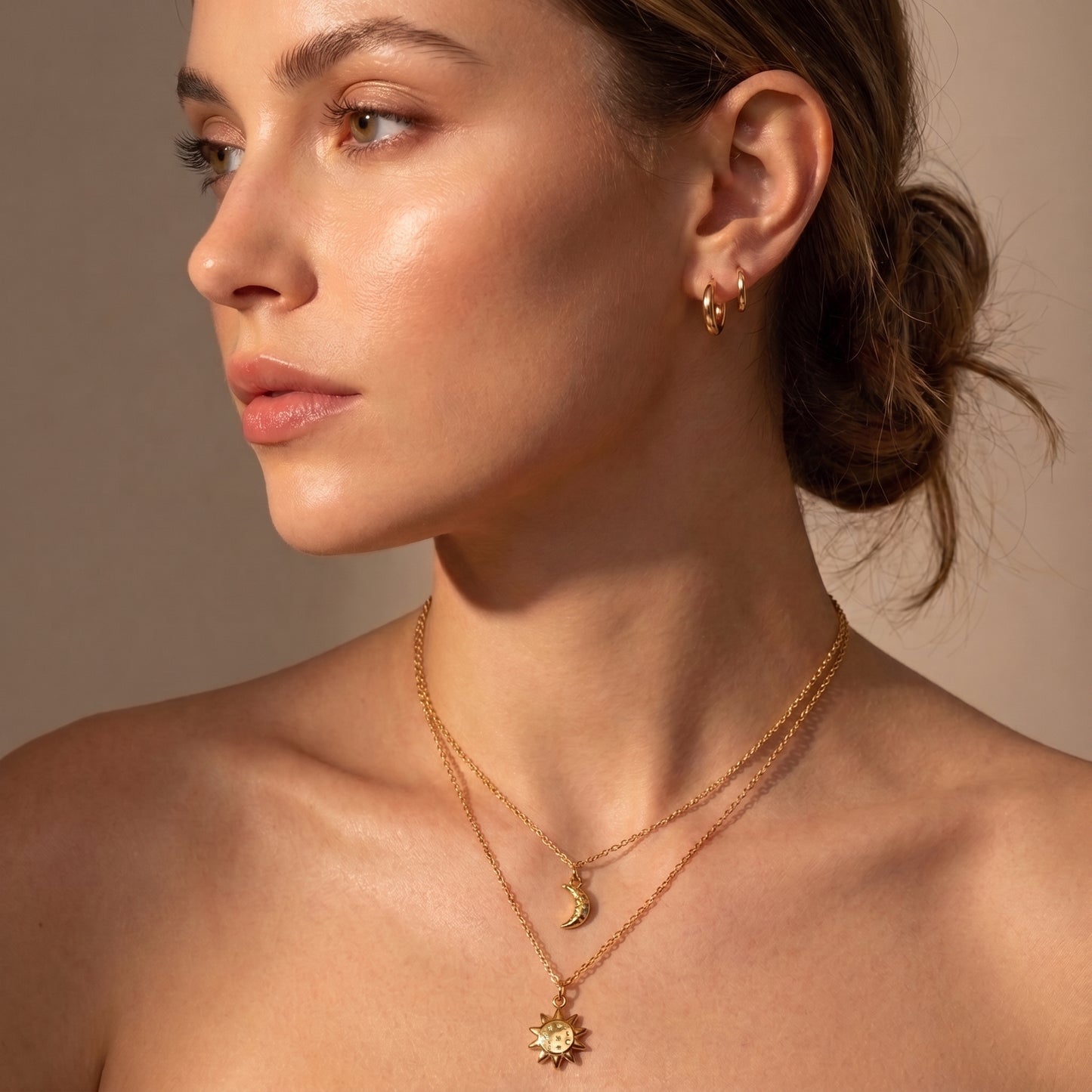 High quality Céleste gold layered sun and moon necklace worn on a model's collarbone paired with minimal gold hoop earrings in warm studio lighting