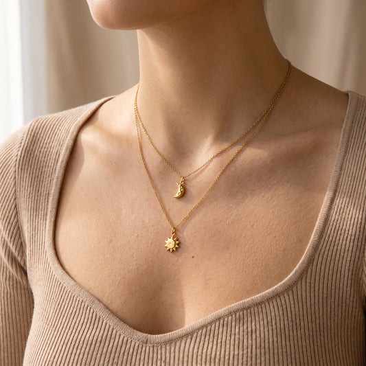 Close-up view of a woman's collarbone wearing the skin friendly Céleste gold layered crescent moon and sunburst necklace with a beige top.