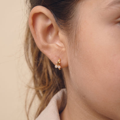 Close-up view of a woman's earlobe wearing the skin friendly Cerise gold pavé cherry huggie hoop earring in soft natural lighting.