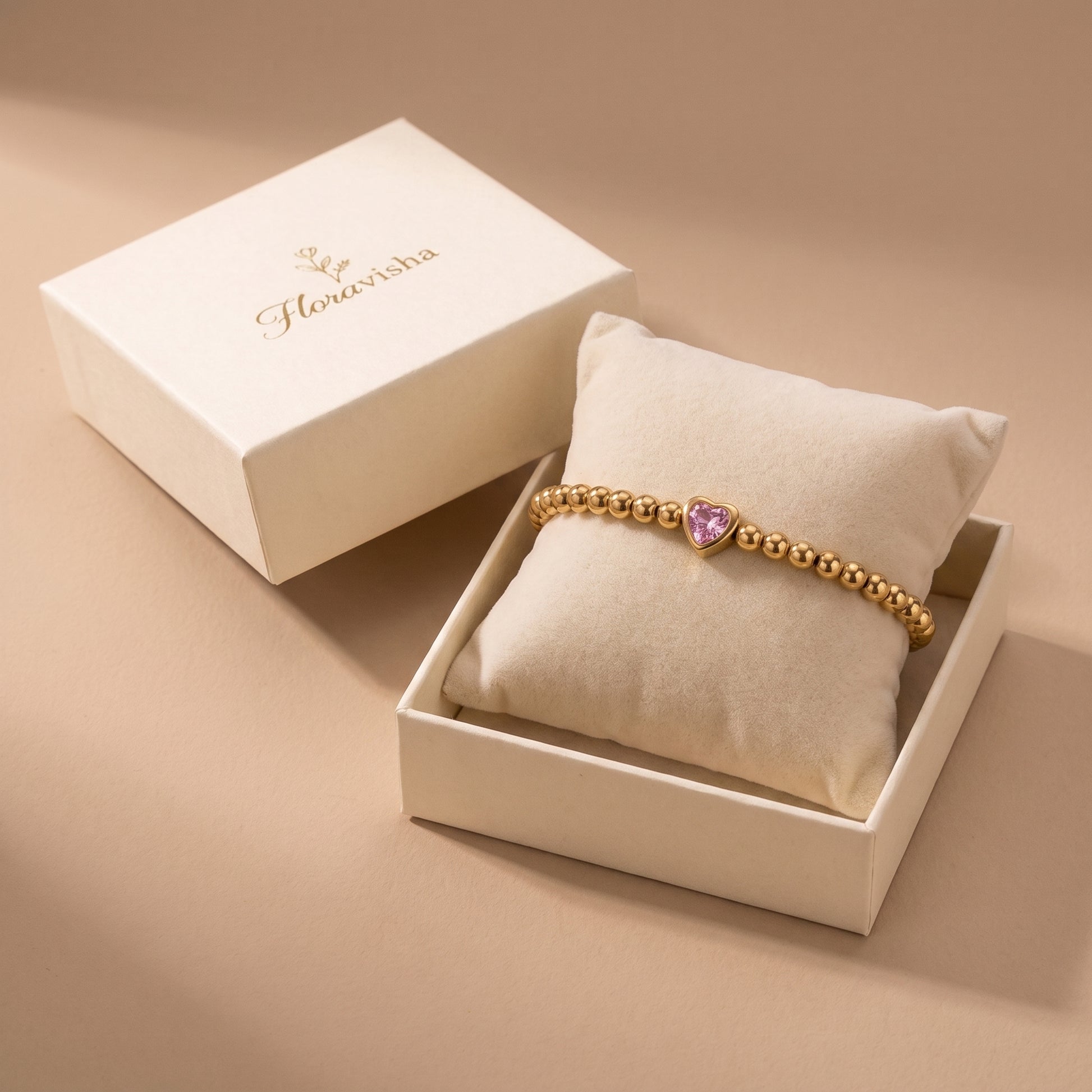High quality Chérie gold pink heart crystal bead bracelet presented on a velvet pillow inside an off-white Floravisha luxury gift box.