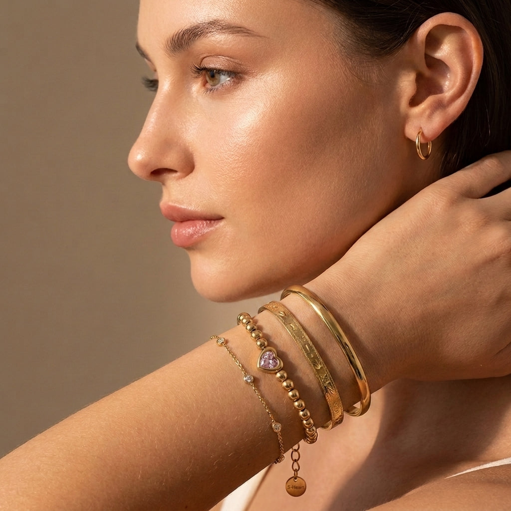 Modern gold wrist stack on a woman featuring the waterproof Chérie pink heart bead bracelet layered with the Astrid engraved cuff and Aura sleek cuff.