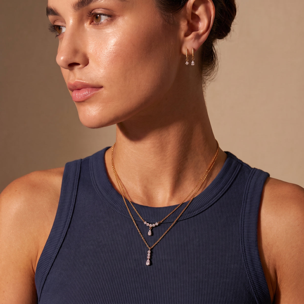 Editorial portrait of a woman wearing the waterproof Clarisse gold crystal arc necklace layered with a drop pendant and paired with Delphine crystal drop earrings.