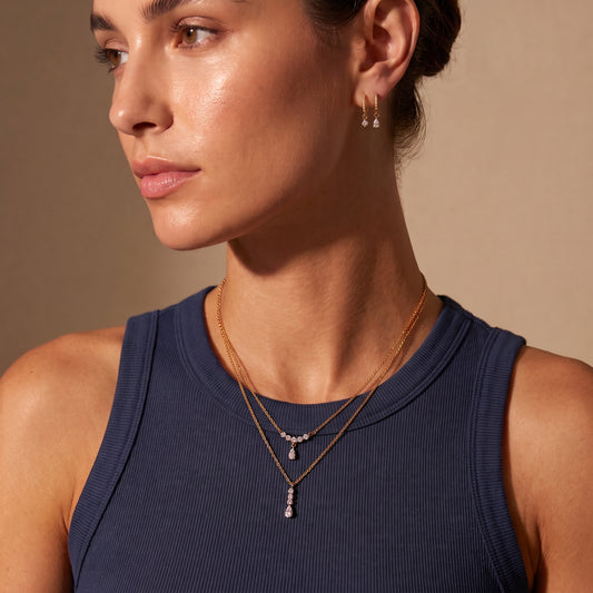 Editorial portrait of a woman wearing the waterproof Clarisse gold crystal arc necklace layered with a drop pendant and paired with Delphine crystal drop earrings.