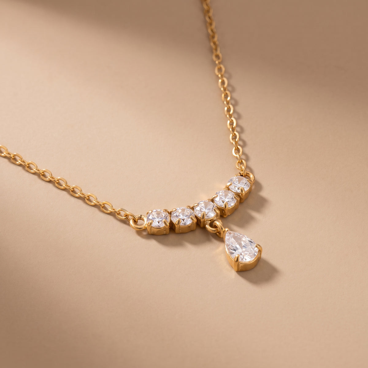 Extreme macro close-up of the tarnish-free Clarisse gold necklace showing prong-set round brilliant cubic zirconia stones and a faceted pear teardrop crystal.