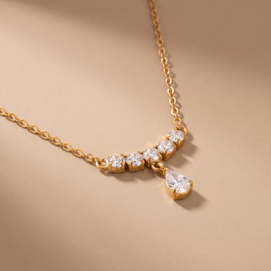 Extreme macro close-up of the tarnish-free Clarisse gold necklace showing prong-set round brilliant cubic zirconia stones and a faceted pear teardrop crystal.