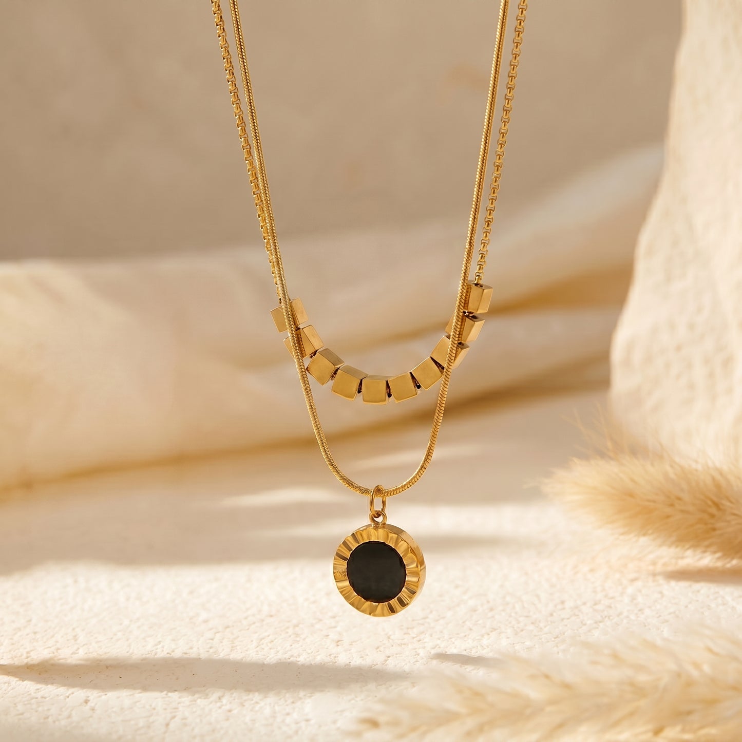 High quality waterproof gold plated double layer necklace featuring gold cube accents and a black natural stone pendant on a beige fabric background