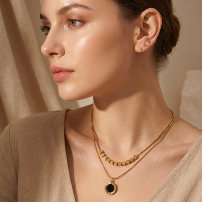 Woman wearing a gold necklace with a black pendant High quality waterproof gold plated double layer necklace featuring gold cube accents and a black natural stone pendant.
