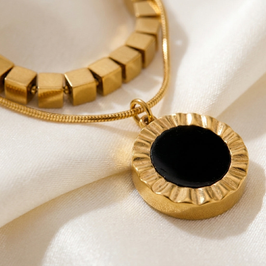 High quality waterproof gold plated double layer necklace featuring gold cube accents and a black natural stone pendant on a beige fabric background