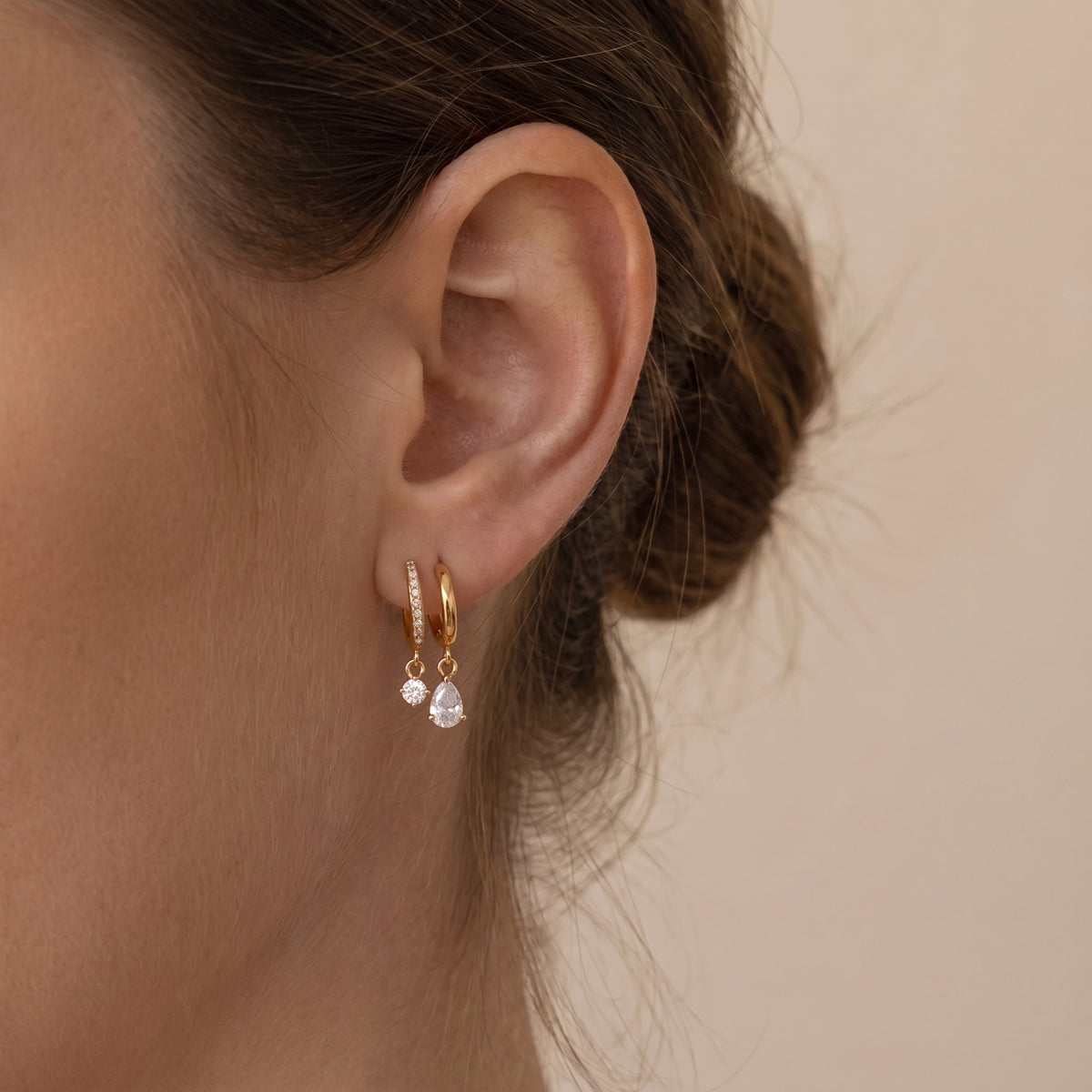 Close-up view of a woman's earlobe wearing the skin friendly Delphine gold dual-arch drop earrings with floating pear and round crystals under natural lighting.