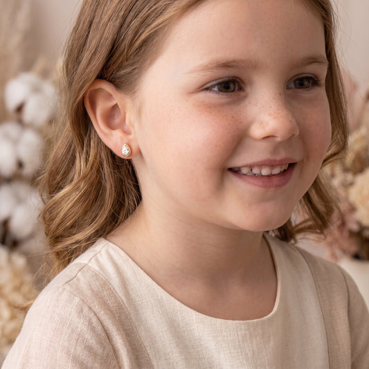 Smiling young girl lying comfortably while wearing the hypoallergenic Delphine Petite gold bezel crystal teardrop stud earrings.