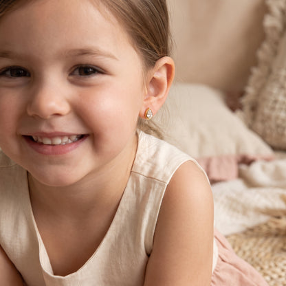 Close-up of a smiling girl with brown wavy hair wearing the lightweight, skin friendly Delphine Petite gold teardrop solitaire stud earrings.