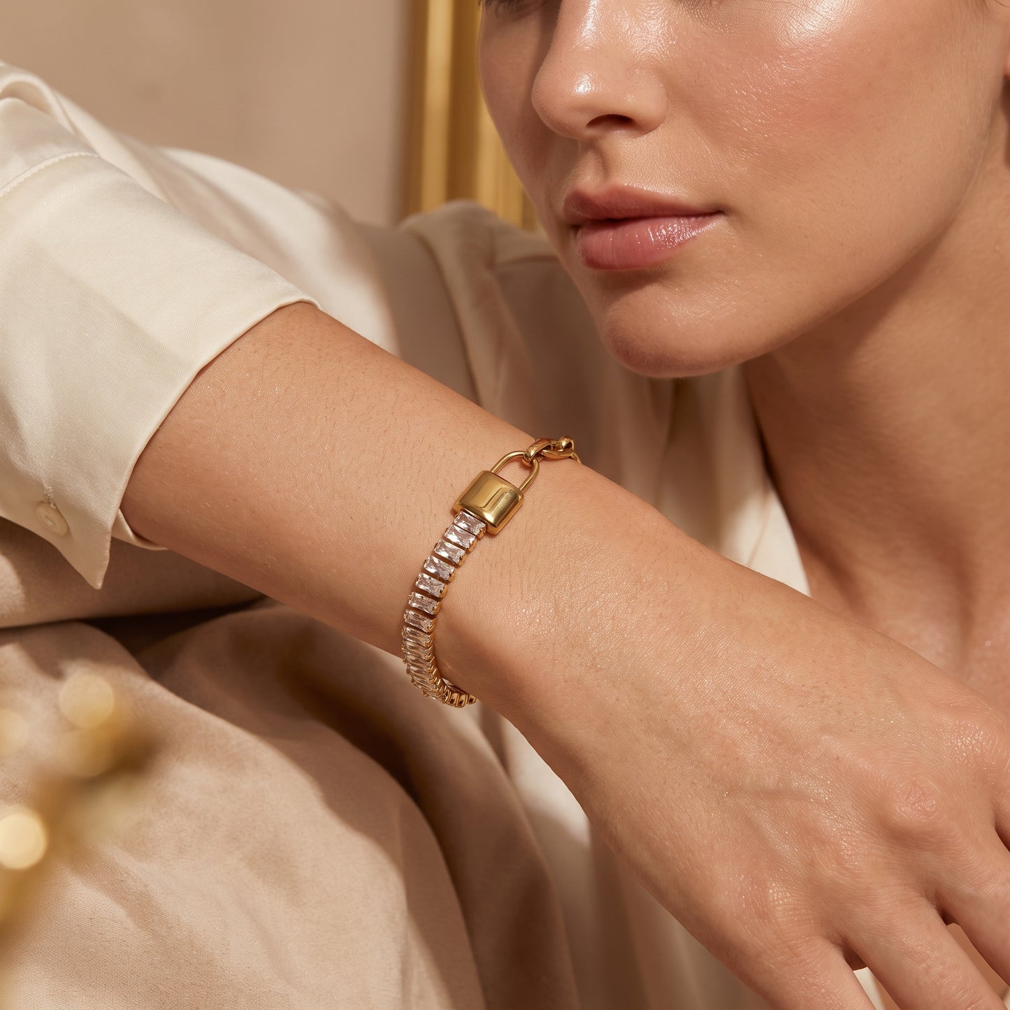 Modern gold wrist drape featuring the tarnish-free Elysée half-baguette crystal half-paperclip chain bracelet on a warm beige background.