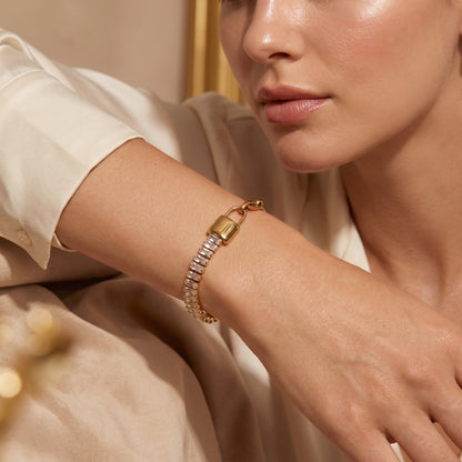 Modern gold wrist drape featuring the tarnish-free Elysée half-baguette crystal half-paperclip chain bracelet on a warm beige background.