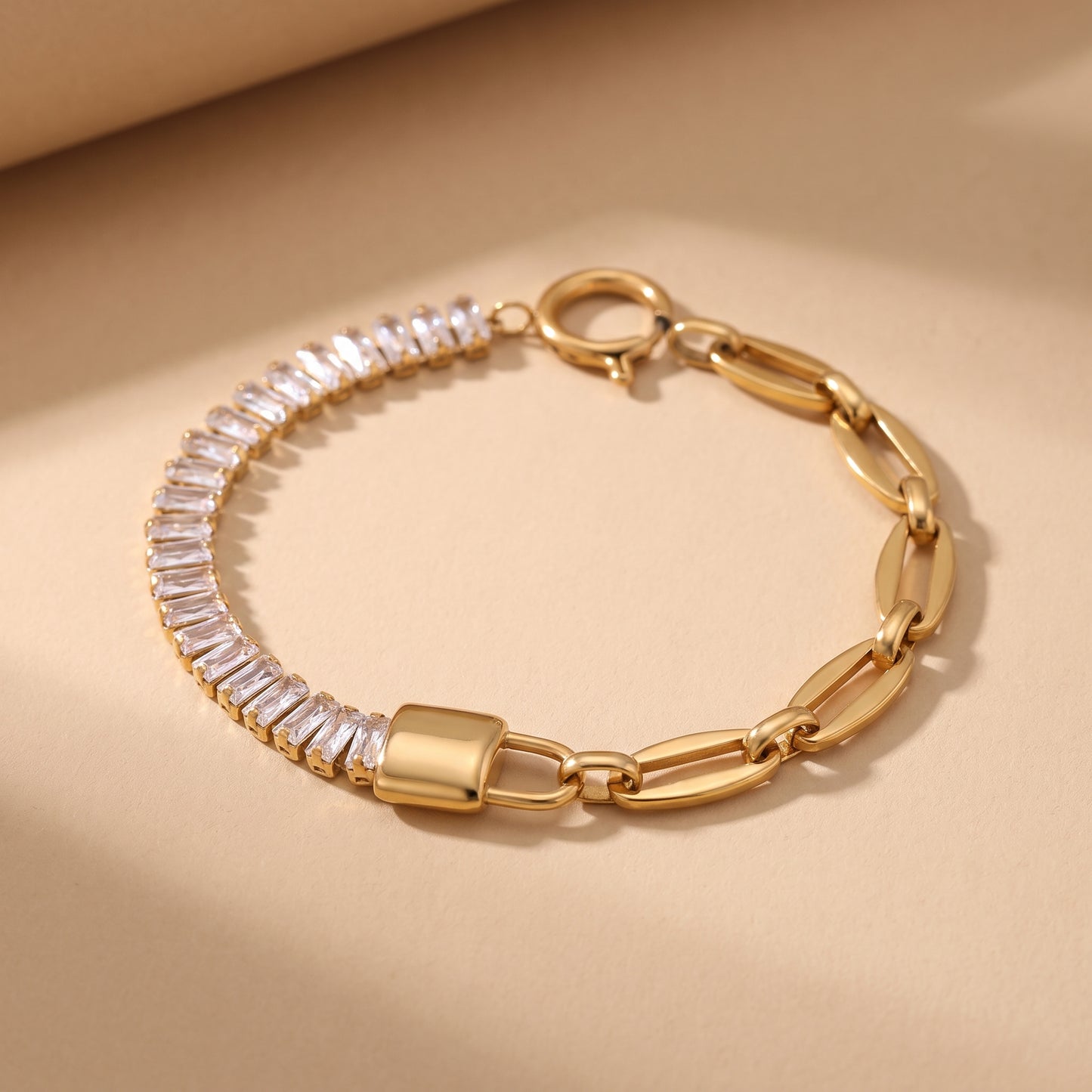 High quality Elysée Gold Bracelet by Floravisha featuring clear baguette crystals, a paperclip chain, and a central gold lock on a warm beige studio surface.