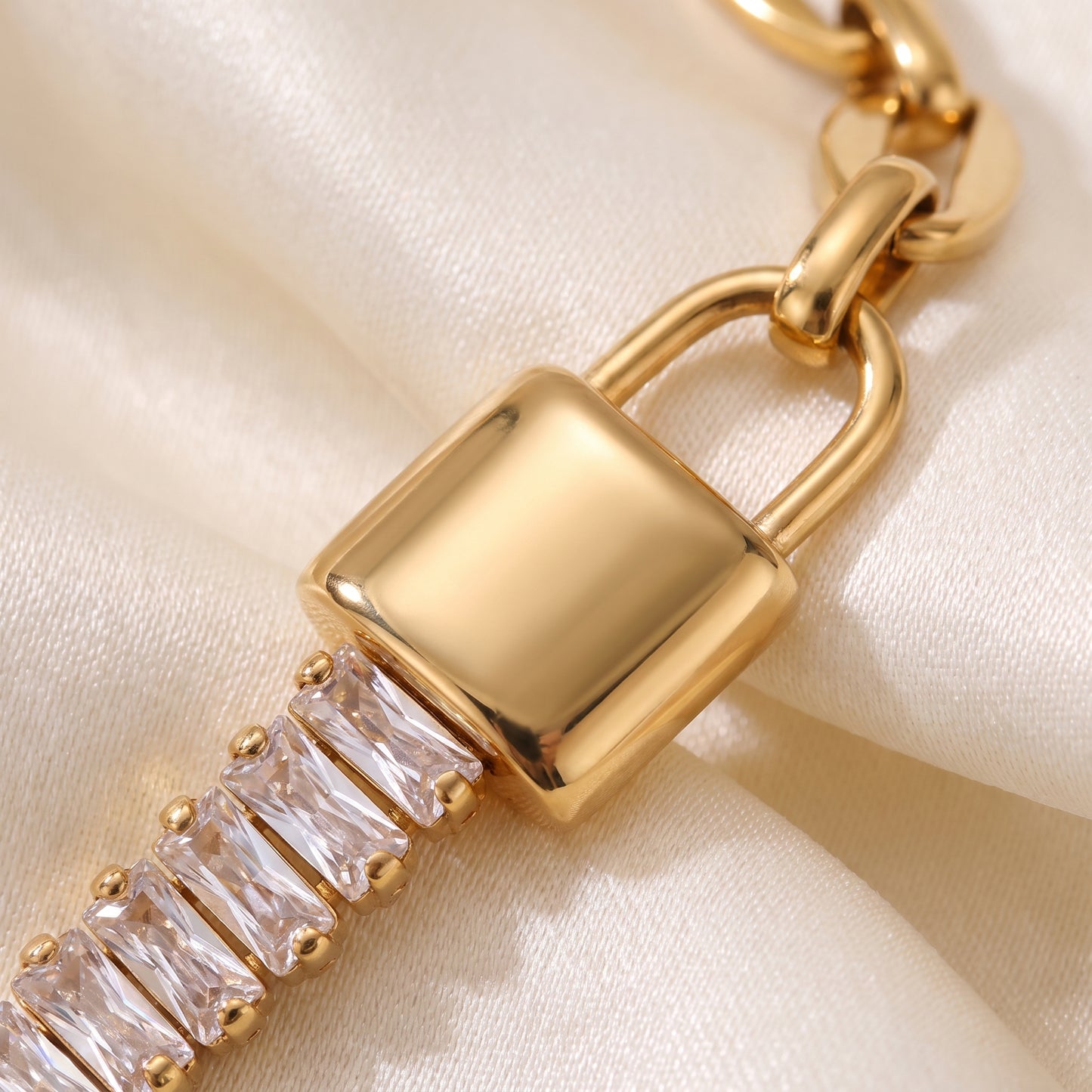 Extreme macro close-up view of the tarnish-free Elysée gold bracelet showcasing the polished gold lock centerpiece and channel-set clear baguette crystals on champagne silk.