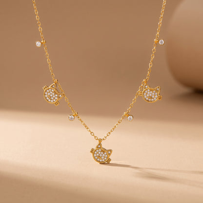 High quality Féline gold pavé cat necklace by Floravisha displaying three crystal cat charms and dangling bezel drops suspended on a warm beige background.