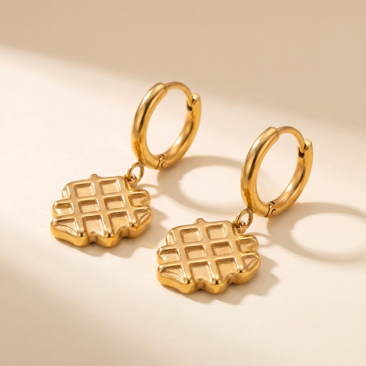 Detailed studio close-up of the tarnish-free La Gaufre gold waffle charm earrings showing scalloped edges and deep grid indentations.