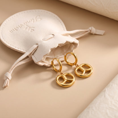 Pair of waterproof Le Bretzel gold pretzel charm huggie earrings displayed beside an off-white Floravisha scalloped suede drawstring jewelry pouch.