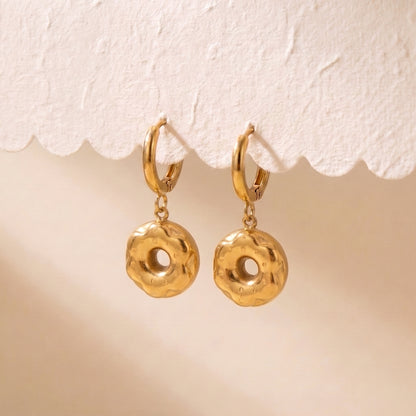 Pair of waterproof Le Donut gold donut charm huggie earrings suspended from a scalloped display card showing balanced drop alignment.