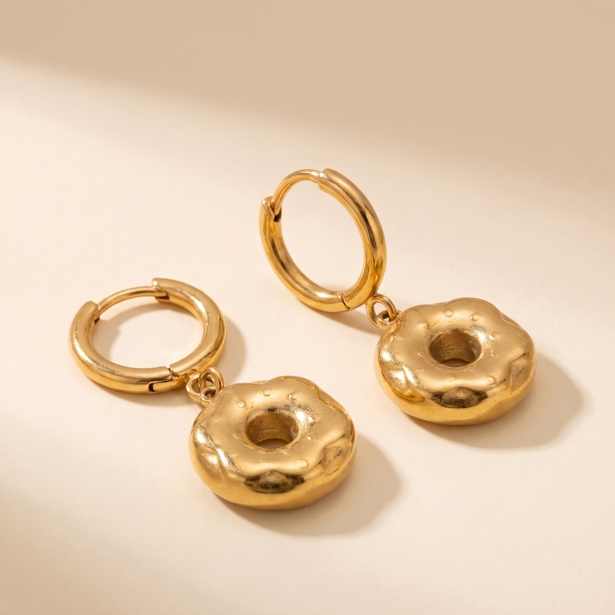 High quality Le Donut gold frosted donut charm huggie hoop earrings by Floravisha showing textured sprinkles and click-hinge clasps on a warm beige surface.