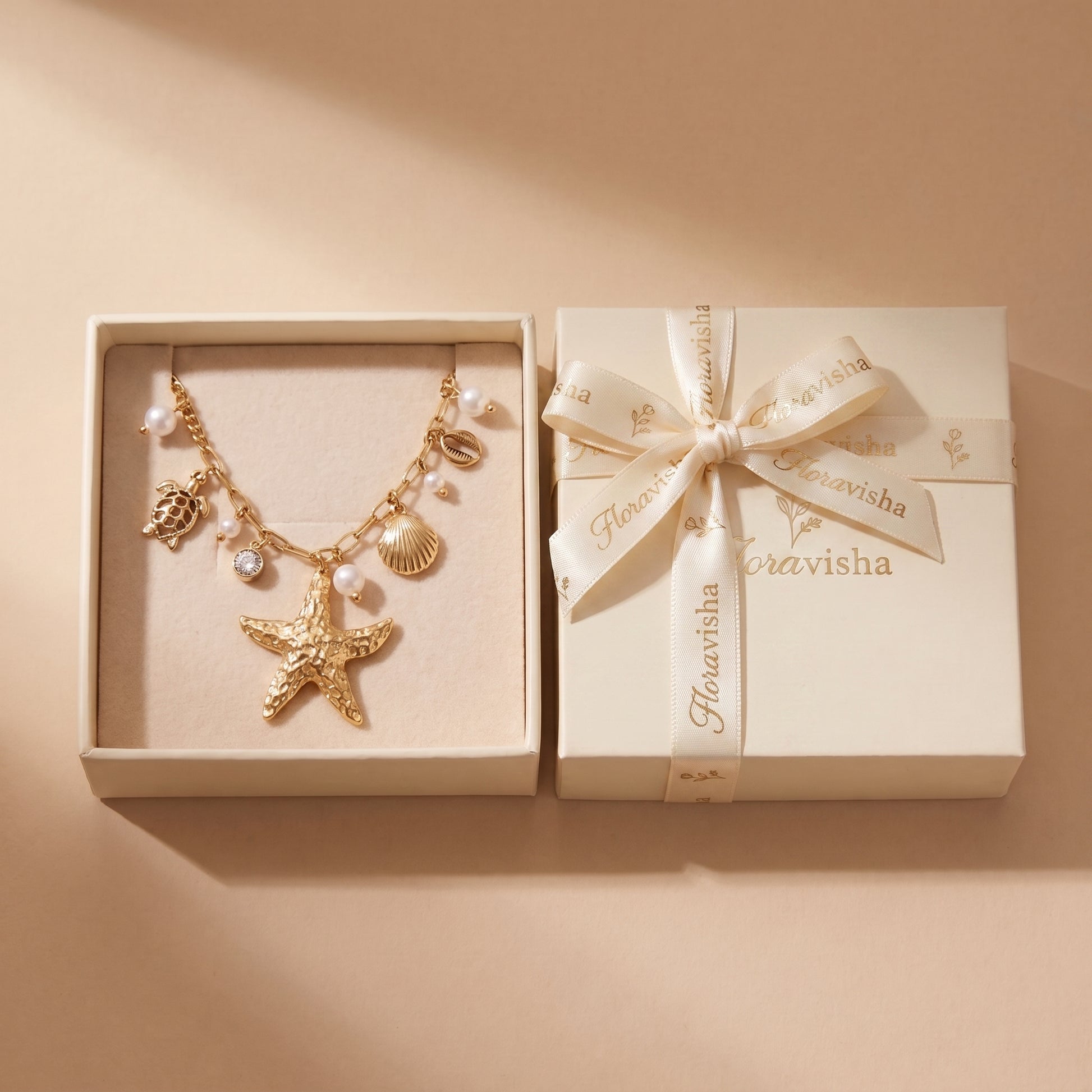 Waterproof Oceane gold coastal charm necklace presented inside an off-white Floravisha luxury jewelry gift box with a ribbon-wrapped lid.