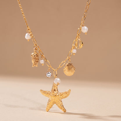 High quality Oceane Gold Necklace by Floravisha featuring a gold starfish, sea turtle, and pearl charms on a warm beige background in direct sunlight.oceane-gold-coastal-starfish-necklace-studio-flatlay.jpg