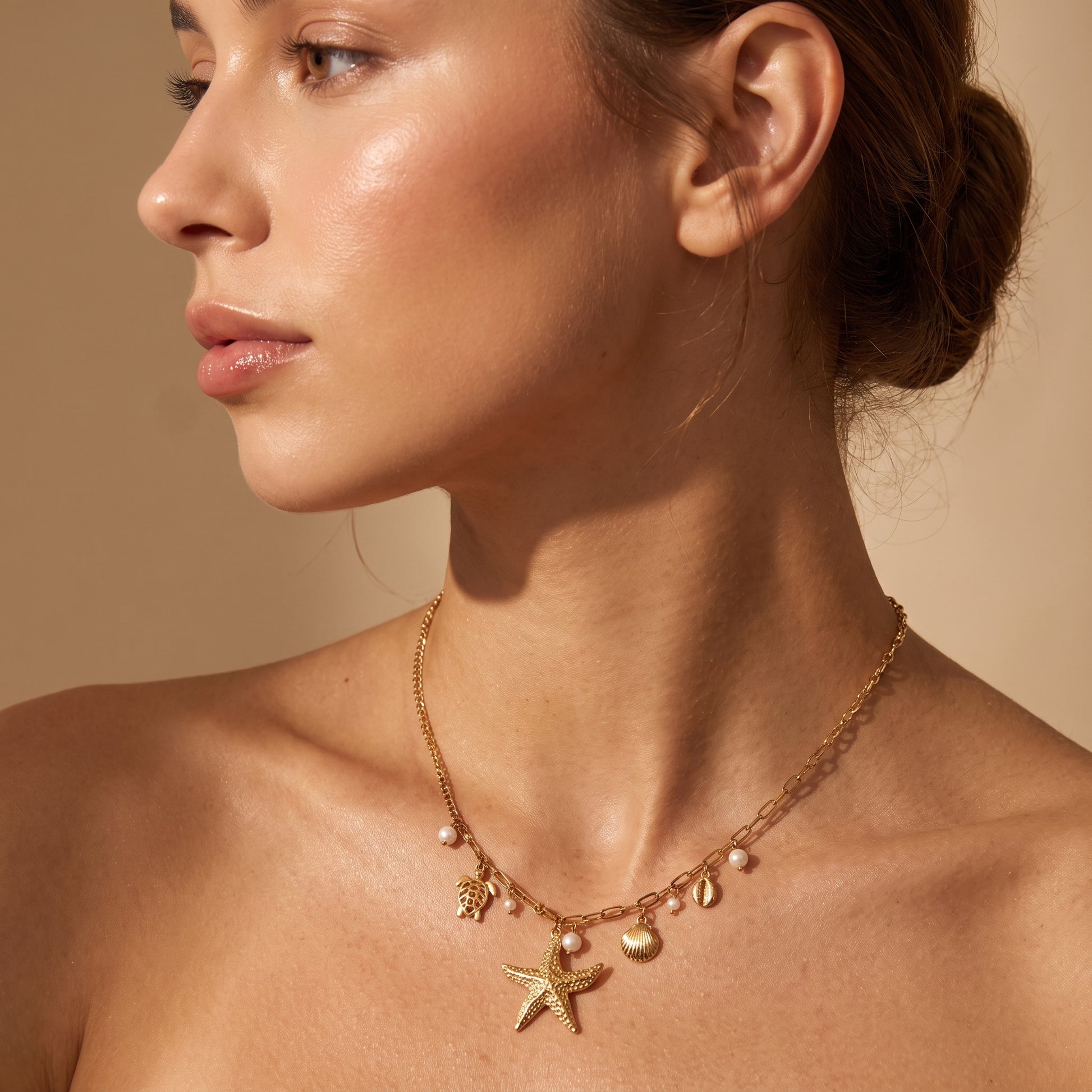 Skin friendly Oceane gold coastal charm necklace with starfish, sea turtle, and pearl drops on a model's collarbone in warm natural lighting.
