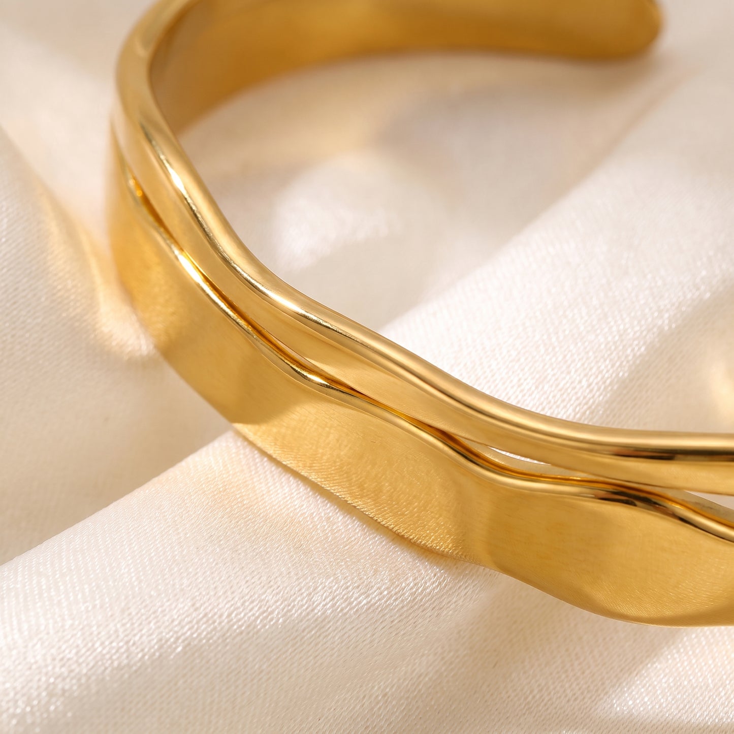 Extreme macro close-up view of the waterproof Ondine gold double wave cuff showcasing mirror-polished molten curves on draped champagne silk.