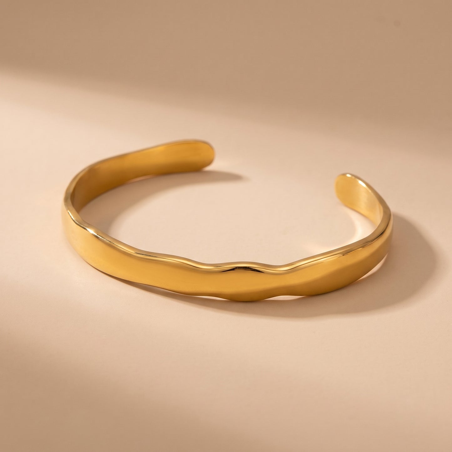 Tarnish-free Statement Ondine gold organic wave cuff bangle displayed on a warm beige background in natural light.