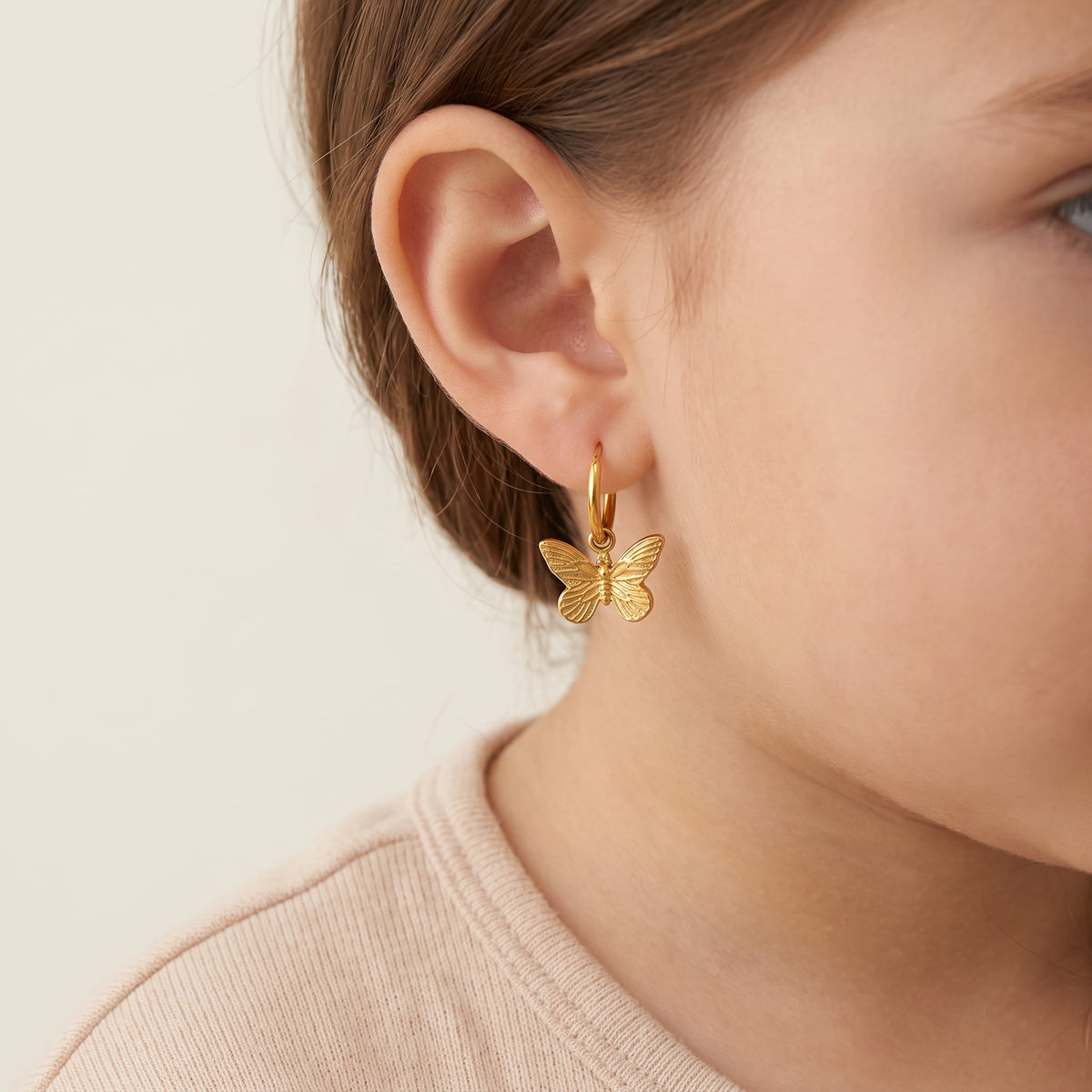 Detailed macro view of a child's earlobe wearing the lightweight Papillon gold butterfly dangle hoop earring showing secure huggie fit.