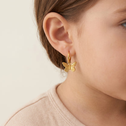Detailed macro view of a child's earlobe wearing the lightweight Papillon gold butterfly dangle hoop earring showing secure huggie fit.