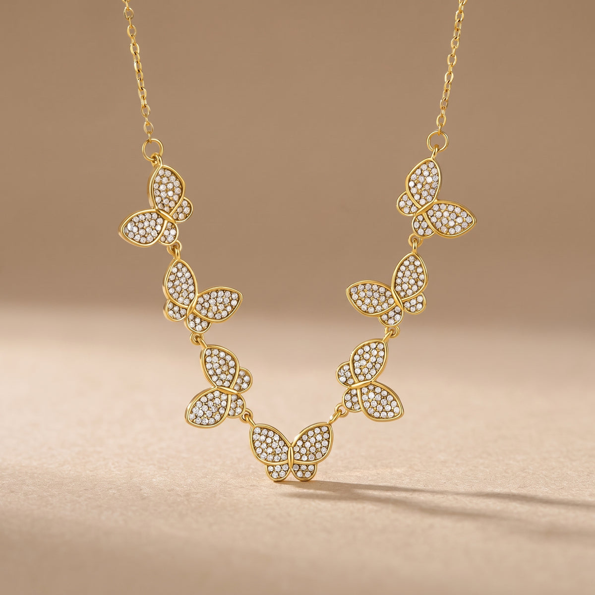 Tarnish-free Papillon gold collar necklace featuring seven linked pave crystal butterfly charms displayed symmetrically on a warm beige background.