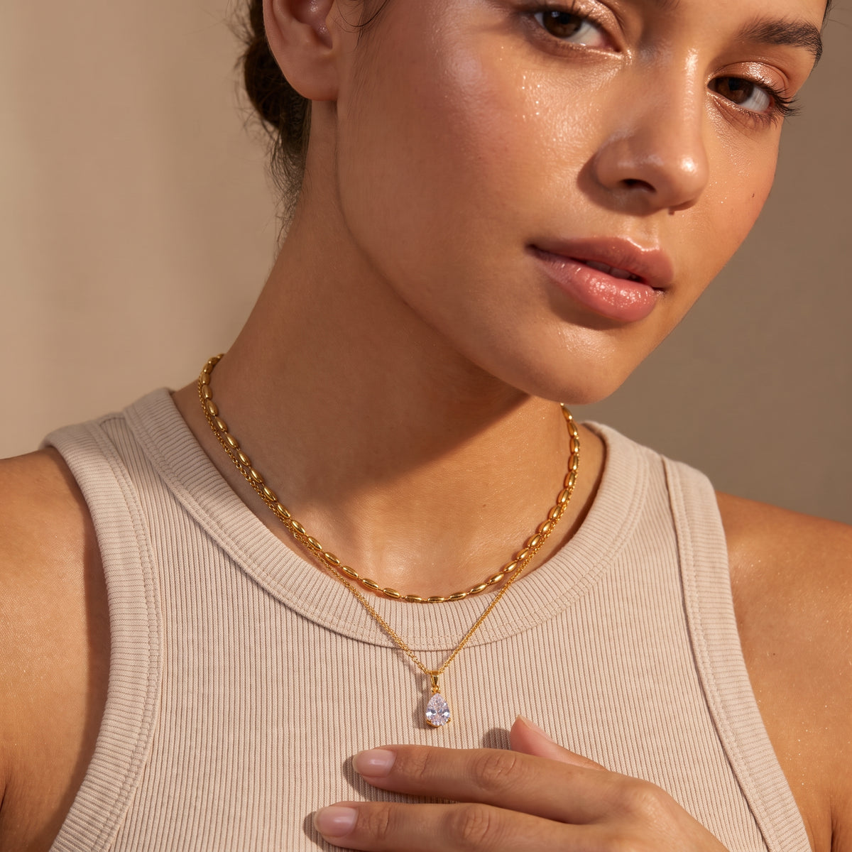 Close-up view of a woman's collarbone wearing the skin friendly Seraphine gold layered necklace with upper oval bead choker and crystal teardrop pendant.