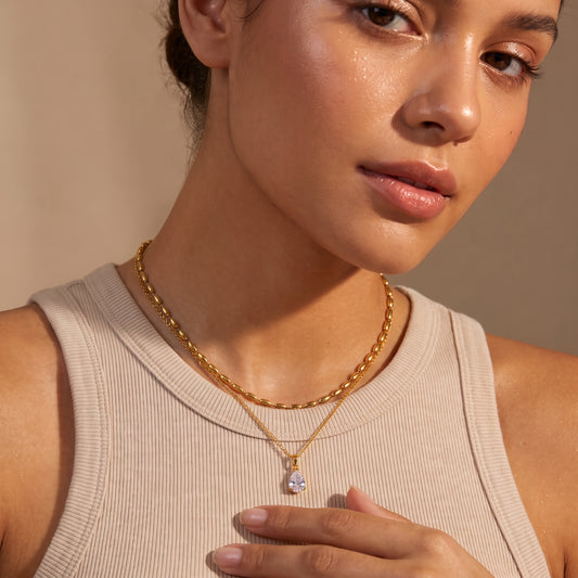 Close-up view of a woman's collarbone wearing the skin friendly Seraphine gold layered necklace with upper oval bead choker and crystal teardrop pendant.