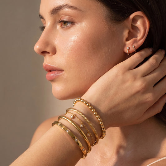 Modern gold wrist stack on a woman's arm featuring the tarnish-free Solene flush-set crystal bracelet layered with pearl beads, a rope cuff, and a tennis chain.