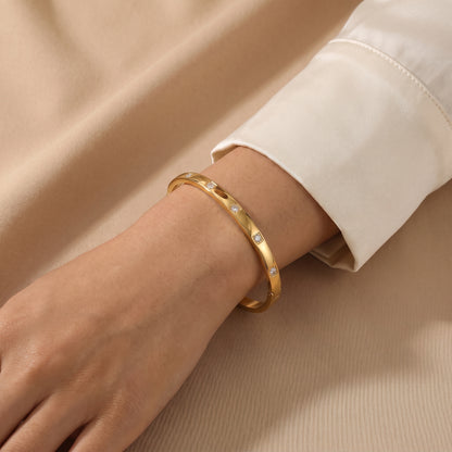 Close-up view of a woman's wrist wearing the skin friendly Solene gold flush-set crystal oval bracelet with a cream silk shirt.